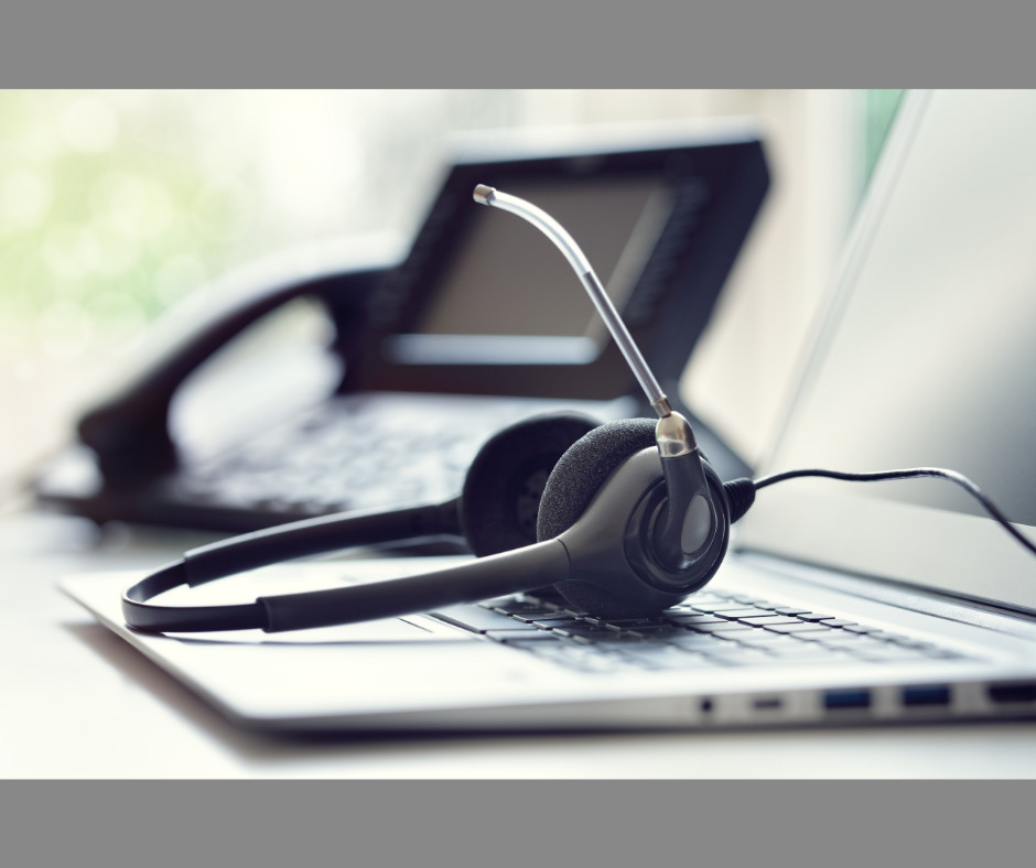 A headset resting on a laptop keyboard with a office phone behind it in the background