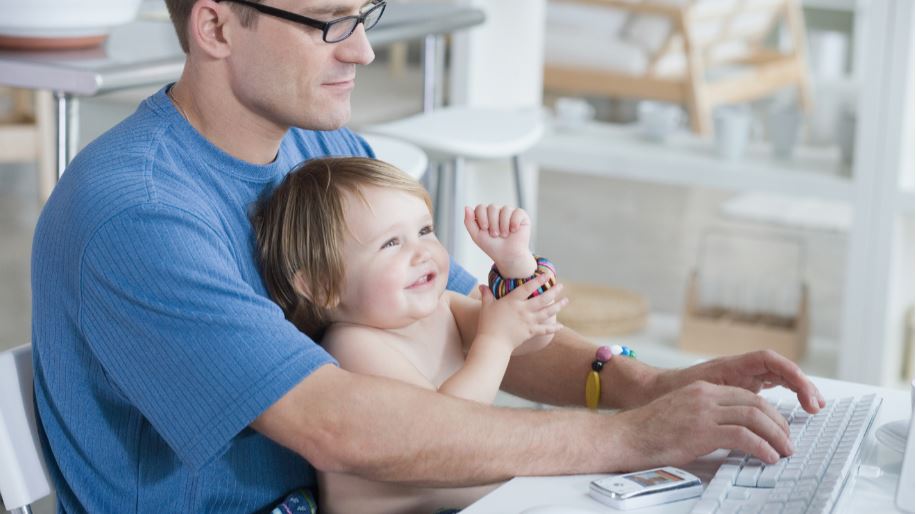 A man using a computer while a baby sits on his lap