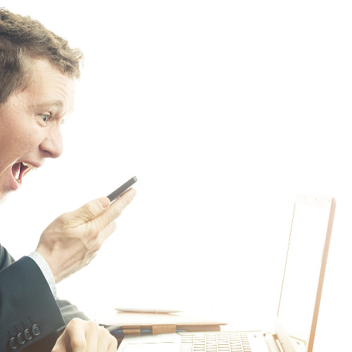 A Man yelling into his mobile phone while sitting infront of a laptop