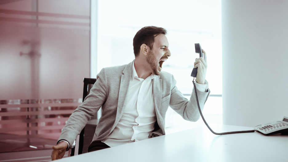 A man in his office yelling into a phone while sitting at his desk