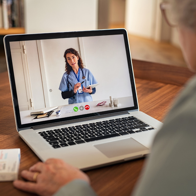 An elderly person using a laptop to video chat with their healthcare provider